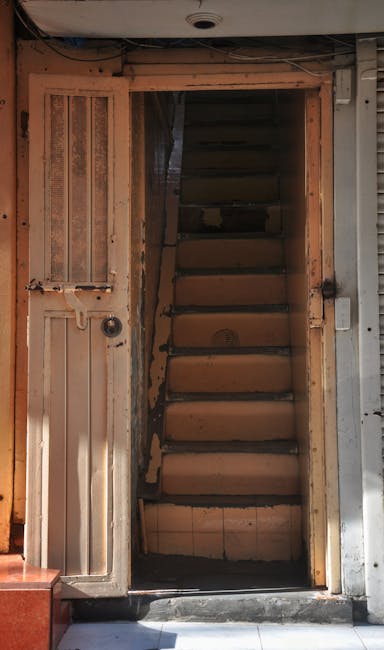 A spiral staircase viewed from below, ascending through multiple levels of a residential property. The staircase features a light wooden handrail and black vertical balusters, contrasting against the