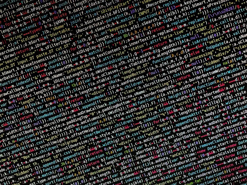 A close-up photograph of a computer screen displaying a coding interface with multicolored lines of HTML, CSS, and JavaScript code on a dark background. Visible elements include layered code snippets 