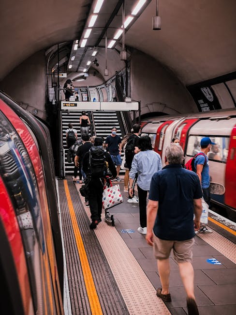 The image shows a busy underground station platform near North Dulwich with several commuters walking towards the stairways and train cars. Passengers are dressed casually, some carrying backpacks and