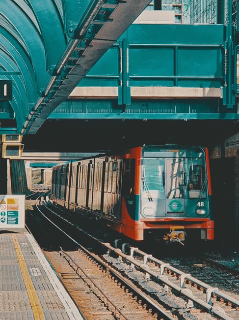 The image shows a busy underground station platform near North Dulwich with several commuters walking towards the stairways and train cars. Passengers are dressed casually, some carrying backpacks and